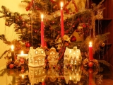 Kerstkaart: Twee kersthuisjes en vier brandende kaarsen staan op tafel voor de kerstboom