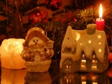 Kerstkaart: Sneeuwpop naast een kersthuisje met daarachter een rode brandende kaars